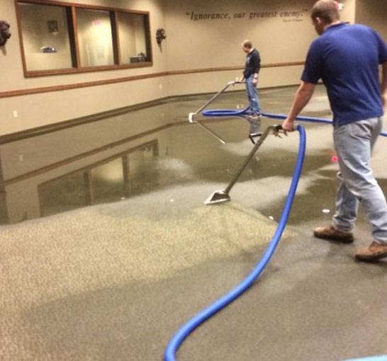 Specialists using high-powered vacuums to perform water extraction. The words "Ignorance, our greatest enemy" hangs in the background. 